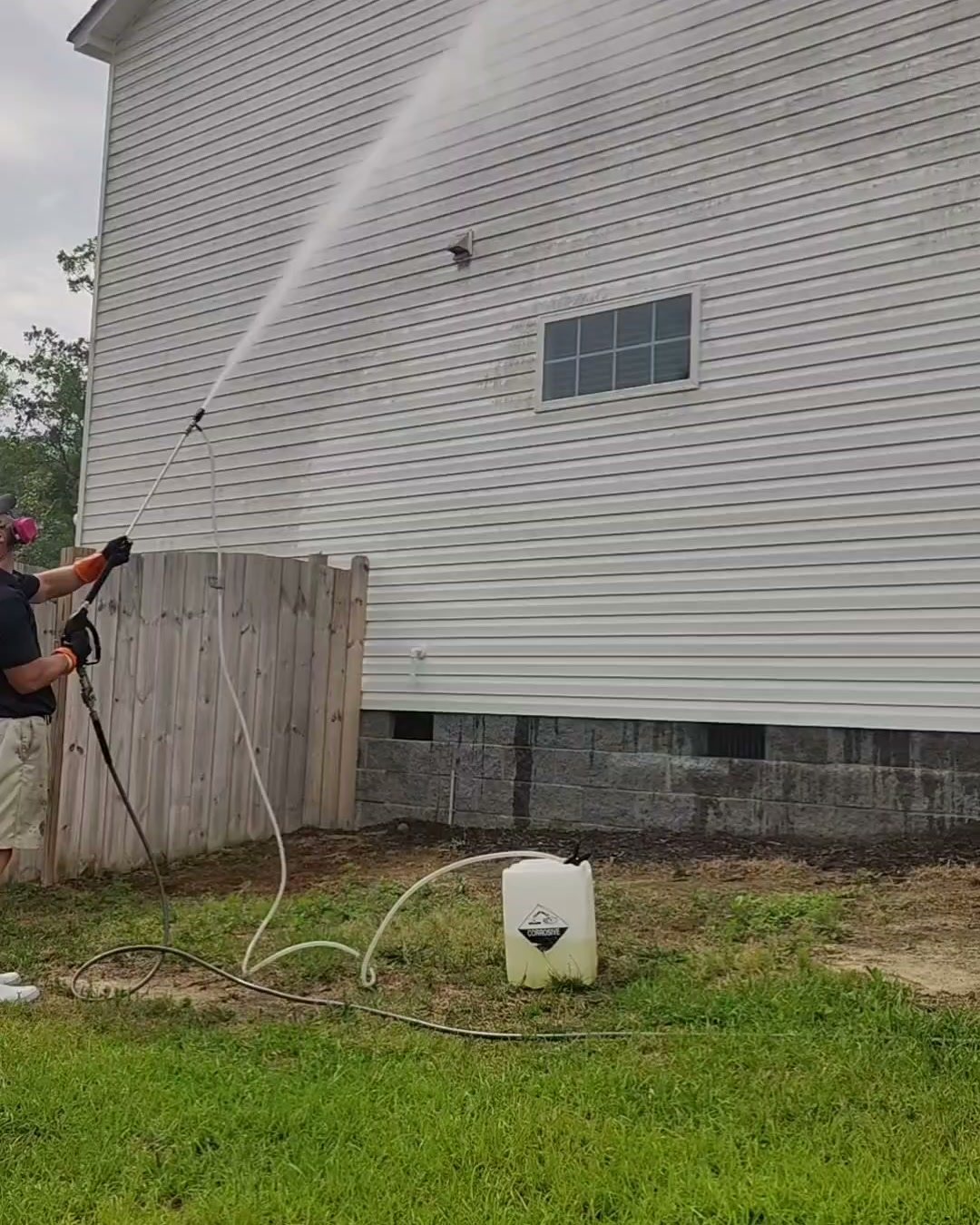 Jeremy soft washing the tall white siding of a two-story house from the ground