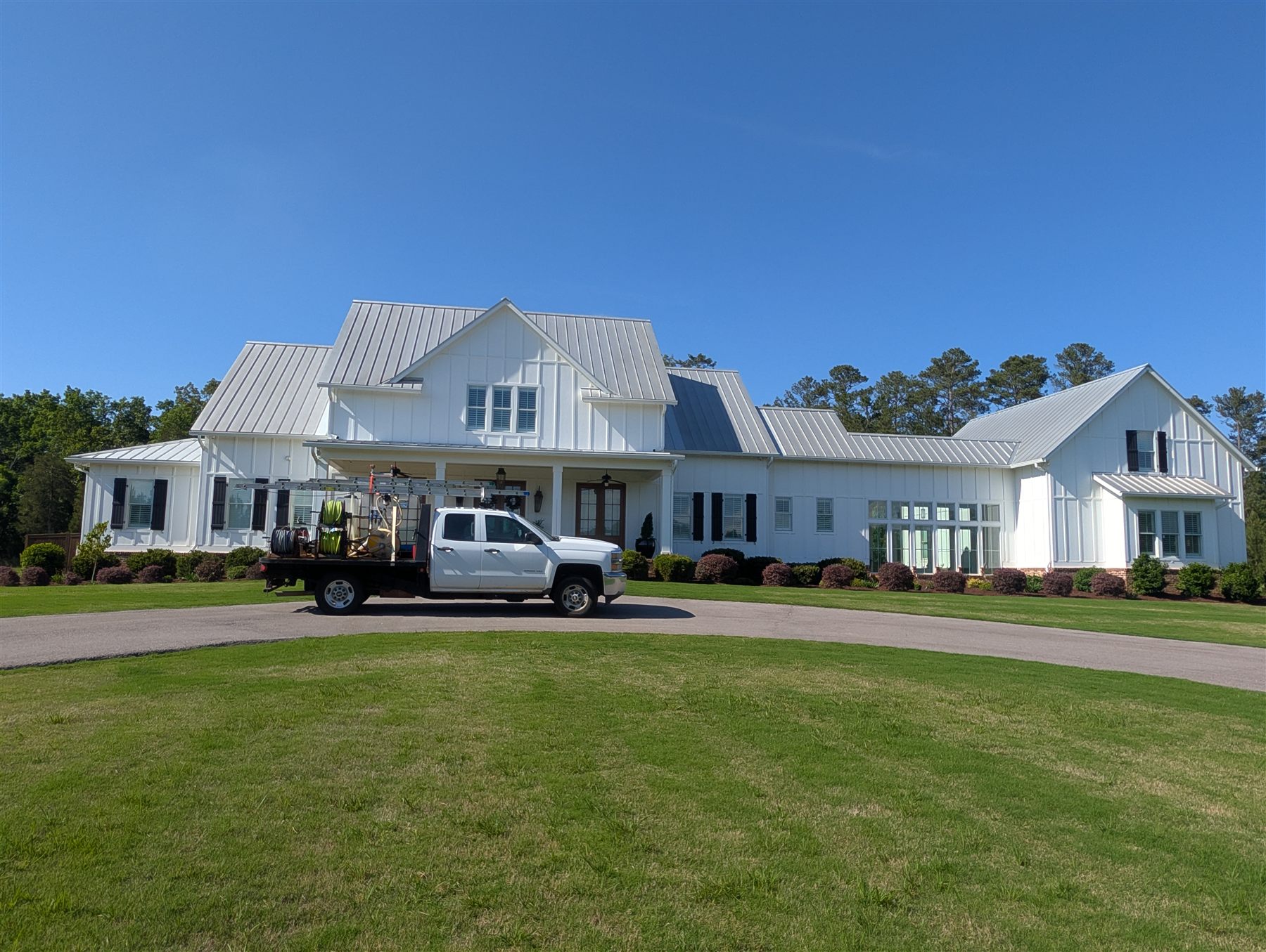 The Soda City truck in the drive of a large white house with a metal roof after a house wash